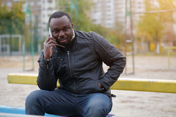 Obraz premium African american man sits at sport ground and speaks on smartphone