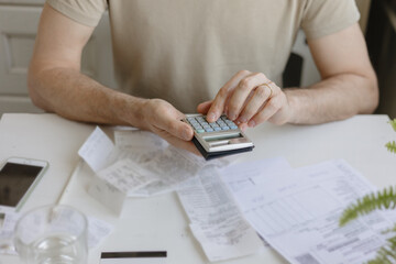 man pays bills and utilities, counts the amount of expenses and income on the calculator. Financial...