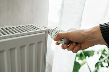 A man regulates the temperature on the radiator at home. Rising prices for heating in households. The concept of the energy crisis in Europe - obrazy, fototapety, plakaty