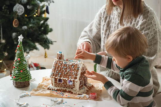 Little Boy With Mother Decorating Christmas Gingerbread House Together, Family Activities And Traditions On Christmas And New Year's Eve