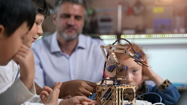 STEM education. A lesson at robotics engineering class. A group of diverse primary school children discussing with their teacher how to assemble and make work electronic robots.