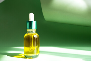 Transparent bottle with serum or cosmetic product on a green background