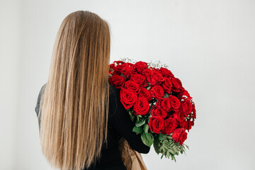 A beautiful young girl with long hair hugging a huge bouquet of a hundred red roses, view from the...
