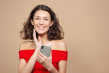Fototapeta premium woman holds a smartphone in her hands and calls or chats with friends. a beautiful woman on a beige background makes phone calls and social media or takes a selfie. modern technologies for work and
