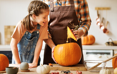 Daughter and dad making Jack-o-Lantern together at home, carving Halloween pumpkin