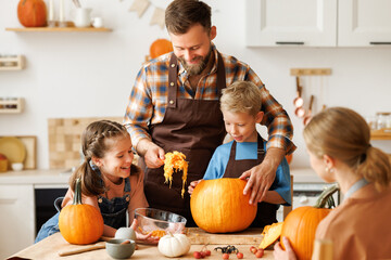 Happy family mother, father and kids  to remove pulp from from pumpkin while carving jack o lantern...
