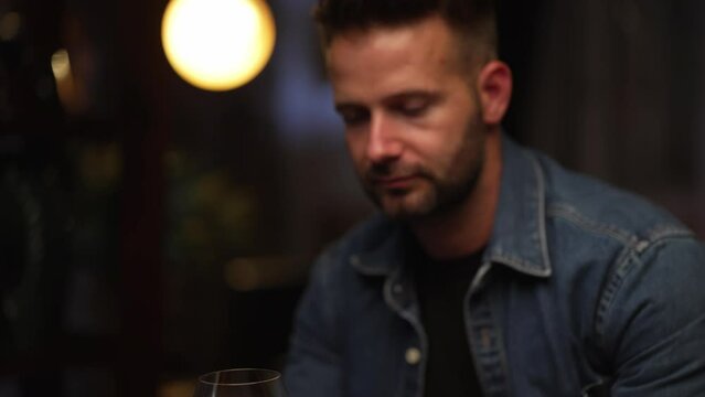 Man sitting in dark room drinking tasting red wine from wine glass.