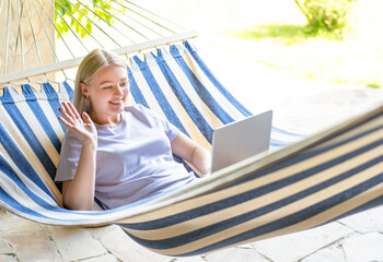 A young girl lies in a hammock with a laptop and communicates through a video call.