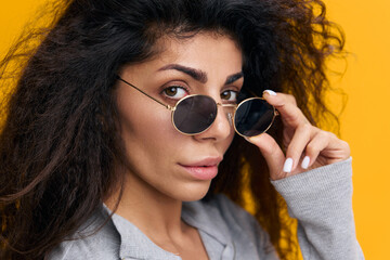 COOL OFFER. Close up portrait of pretty Latin female with afro in sunglasses, look at you, stay isolated over yellow background. Copy space, free place, banner for fashion sale