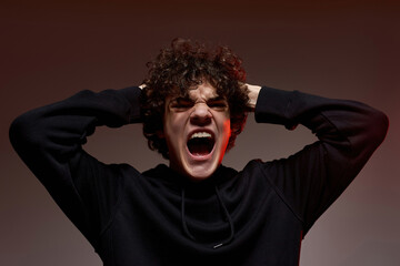 Aggressive teenage boy holding head and screaming