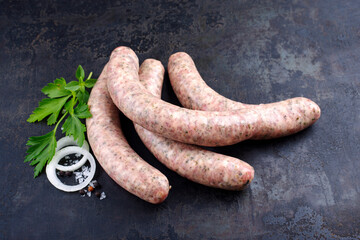 Rohe grobe Allgäuer Bratwurst garniert mit Kräutern und Gewürzen als close-up auf rustikalen...