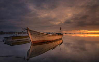 Solo fisher boat on foreground and colorful sunset sky on background 