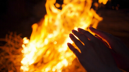 Female person tries to warm up hands near campfire flame - obrazy, fototapety, plakaty