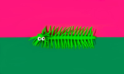 A green caterpillar on the border between magenta and green background.  Minimal surreal concept for Halloween celebration banner or print. Surreal Autumn holidays design for advertisement