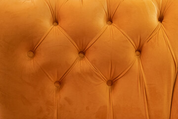 close-up view of soft velvet back of orange sofa with decorative buttons