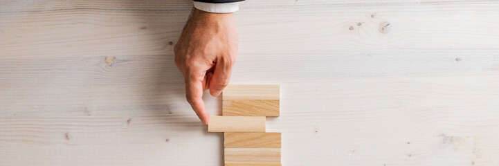 Top view of male hand in a suit pushing a blank wooden peg into a stack of them