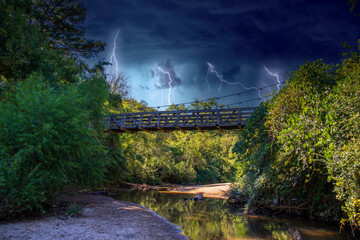 a brown wooden suspension bridge over the clear waters of the South Fork Peachtree Creek surrounded...