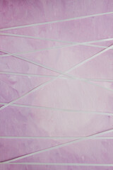 Pink painted canvas wrapped with white ribbon in many directions; white ribbon wound around canvas...
