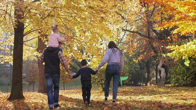 Happy family walking together in the autumn park. Mom, dad, daughter and son walk holding hands on autumn leaves outdoors in city park. Parenthood, carefree childhood, love and happy family concept.