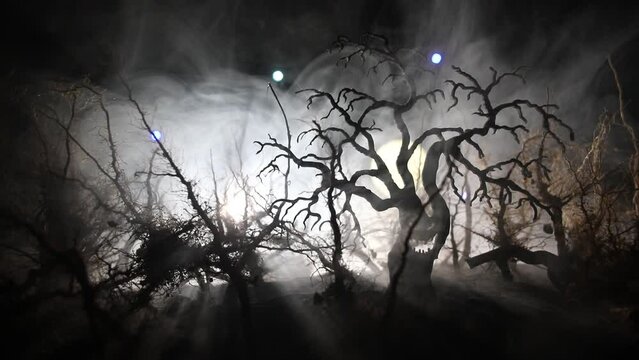 Spooky dark landscape showing silhouettes of trees in the swamp on misty night. Night mysterious forest in fire and dramatic cloudy night sky