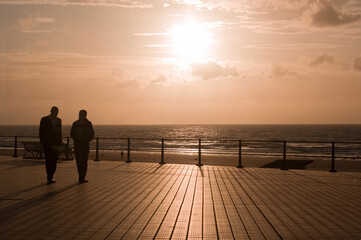 silhouettes of a pair of male friends walking along the terrace in the sunset
