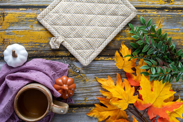 Cozy coffee autumn flat lay arrangement, with pumpkins, pot holder and maple leaves on a yellow rustic wood background