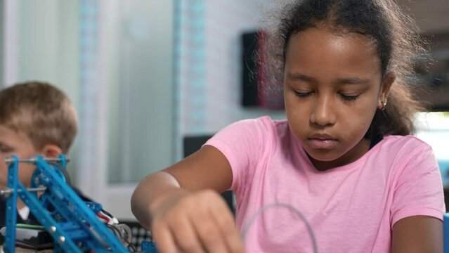 Close up of brilliant african elementary school girl attentively watching how her robotic crane working at robotics engineering laboratory. School science classroom of futuristic technologies. STEM 