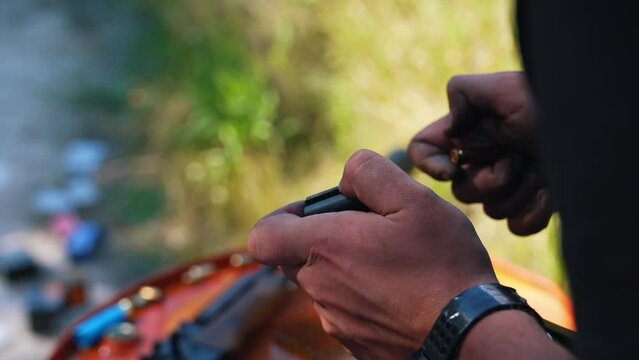 Unrecognizable caucasian person's hands placing golden shotgun shells or bullets in clip magazine. Outdoor shot. Shooting range concept. Blurred background. High quality 4k footage