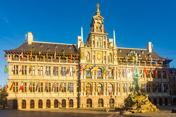 Fototapeta na wymiar View of Brabo fountain and four-story Renaissance building of Antwerp City Hall with main facade lavishly decorated with sculptures and waving flags located on central Grote Markt square, Belgium..