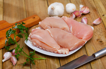 Uncooked raw chicken breast fillet with parsley and garlic on wooden table