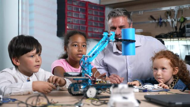 Enthusiastic teacher and diverse children watching on working robotic electric machine they made at robotics engineering class. School science classroom of futuristic technologies. STEM education 