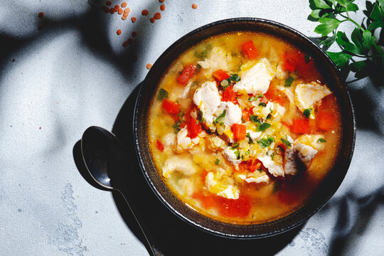 Warming autumn soup with red lentils, chicken fillet, vegetables, spices and paprika, comfort food. White table, hard light with leaf shadows, top view