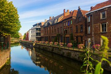 Scenic cityscape of Ghent with traditional Flemish style brick townhouses decorated with colorful blooming flowers on banks of Leie river on sunny summer day, Belgium..