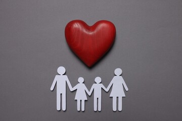 Paper family figures and red wooden heart on grey background, flat lay. Insurance concept