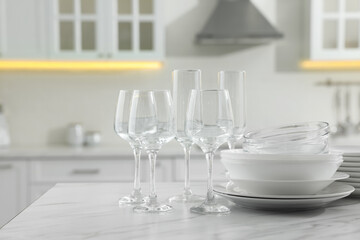 Different clean dishware and glasses on white marble table in kitchen