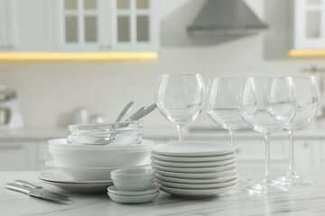 Fototapeta na wymiar Different clean dishware, cutlery and glasses on white marble table in kitchen