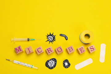 Word Microbes made with wooden cubes, pictures, syringe and thermometer on yellow background, flat lay. Space for text