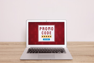 Laptop with activated promo code on wooden table near white wall