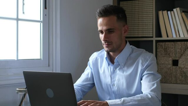 Happy Young Caucasian Millennial Businessman Working At Home At Desk With Laptop Or Computer Having Fun. Young Male Person In Video Conference Taking Care Of The Business Or Market.