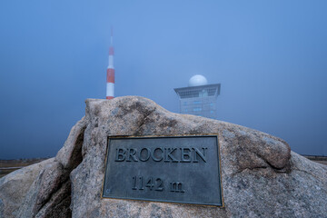 Schild mit Höhenangaben des Brocken, mit Fernsehturm und Brockenhotel im Hintergrund