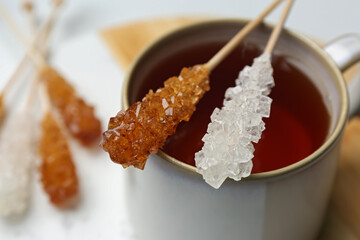 Sticks with sugar crystals and cup of tea on table, closeup
