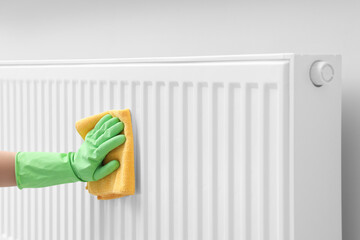 Woman cleaning radiator with rag indoors, closeup. Space for text