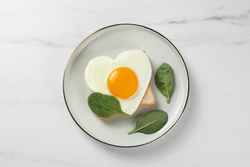 Romantic breakfast with heart shaped fried egg on white marble table, top view