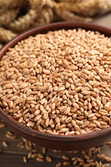 Wheat grains in bowl on wooden table, closeup