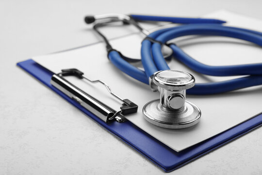 Clipboard with stethoscope on white background, closeup