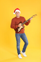 Naklejka premium Man in Santa hat playing electric guitar on yellow background. Christmas music