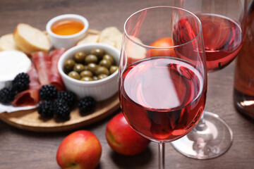 Delicious rose wine and snacks on wooden table, closeup