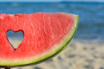 Child holding slice of watermelon with heart shaped hole near sea, closeup