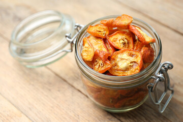 Glass jar with cut dried kumquat fruits on wooden table, closeup