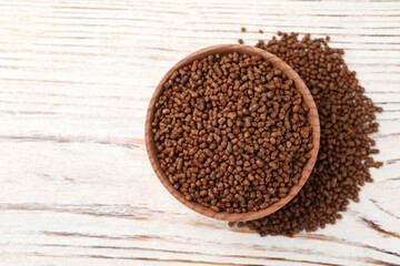 Bowl with buckwheat tea granules on white wooden table, top view. Space for text